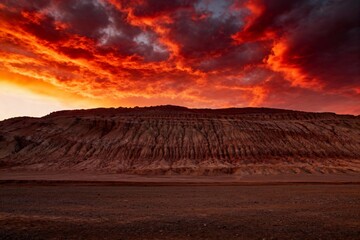 Dramatic red sunset over a desert landscape with layered rock formations and fiery clouds