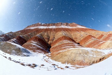 Snow-covered layered rock formations under a clear blue sky with falling snow