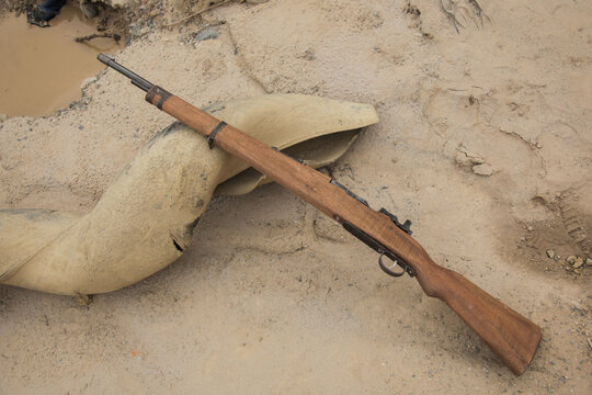 
A rifle lying on a pipe in the sand. It looks like a rustic, abandoned place where a paramilitary or soldier walks away, leaving his weapon behind
