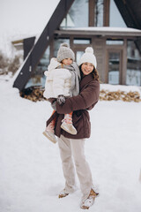 Mother holding child enjoying winter snow outside cabin