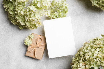 Blank greeting card mockup with gift box and dried hydrangea flowers on textured surface, ideal for personalized messages and creative designs with copy space