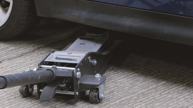 Close up car jack lowering vehicle. Loud squeaking and creaking sound as car suspension engages. Sync audio