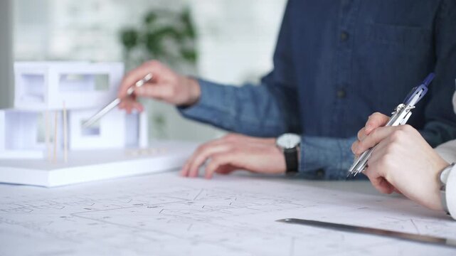 Architects collaborating on blueprint plans, discussing engineering details and project designs, planning construction development with a laptop in a modern office environment