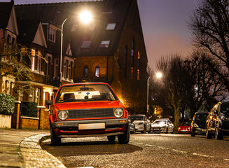 Obraz premium Vintage red car on cobblestone street at night in European city neighborhood