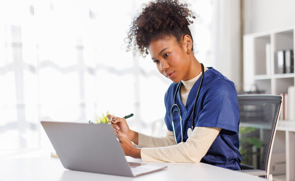 Nurse, young female doctor using laptop online, writing notes in medical journal sitting at desk, professional medic physician working on computer at workplace, med student learning, planning


