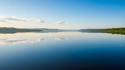 Fototapeta premium Serene landscape view of a vast calm lake with a perfect mirror reflection of the blue sky and soft white clouds.