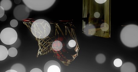 Passing basketball through worn net, rim glowing by wooden backboard at gym court with bokeh lights