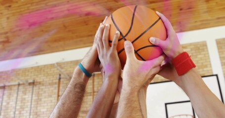 Reaching cluster of four arms grasping orange basketball at gym court with teal and red wristbands