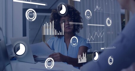 Reviewing analyst in blue blouse and glasses holding documents in conference, with laptop overlays