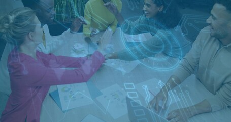 Working team leaning in at meeting table, wearing business casual, using laptop and hologram charts