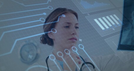 Viewing woman doctor gazing at holographic interface in clinic, wearing white coat and stethoscope