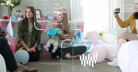 Holding infant with bright bib, woman in striped top sitting on carpet, with balloons, cake, phone