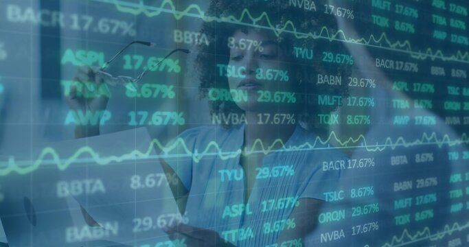 Studying two analysts reviewing stock data on glass wall at office, in blouses holding glasses - Powered by Adobe