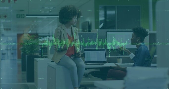 Discussing female colleagues wearing blazer and button-up at modern office, with laptops and coffee - Powered by Adobe