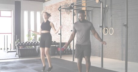 Skipping partners wearing black crop top and gray t-shirt in fitness studio, with jump ropes