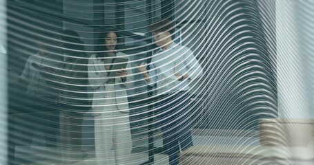 Reviewing tablet, two colleagues pointing behind patterned wavy glass partition in office, in suits