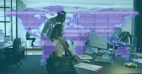 Leaning manager guiding seated analyst using mouse at open-plan office, sleeveless top, purple map