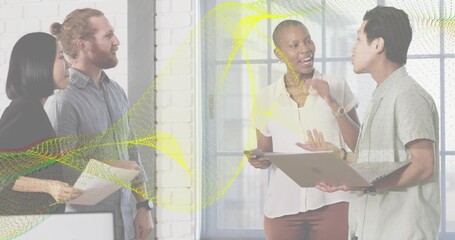 Talking team of four in office attire near window, brick column, with docs or laptop or phone or wav