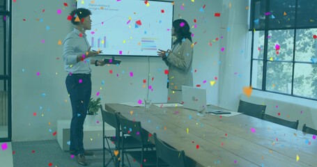 Presenting coworkers in business-casual gesturing at wall screen in meeting room, with confetti