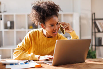 Business woman using laptop calling phone at office desk. talking smartphone read financial graph chart Planning marketing info. Happy African american in afro hair business people work office firm
