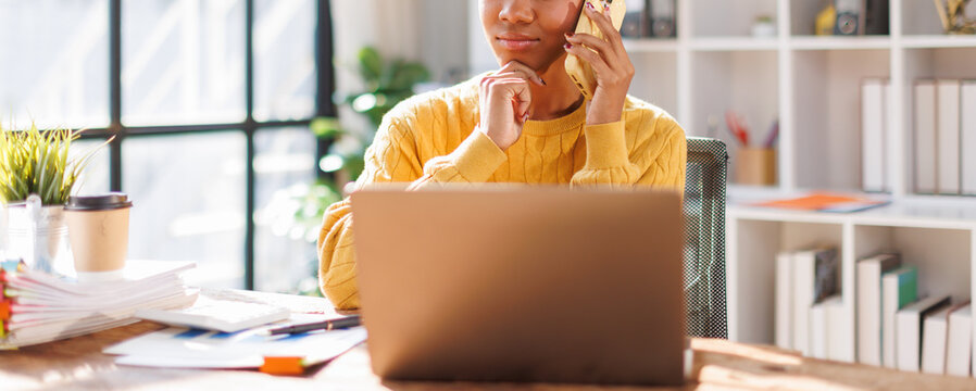 Business woman using laptop calling phone at office desk. talking smartphone read financial graph chart Planning marketing info. Happy African american in afro hair business people work office firm
 - Powered by Adobe