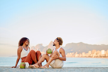 Fototapeta premium Young couple sitting on concrete wall, enjoying fresh coconut water with Two Brothers Mountain in the background, Rio de Janeiro