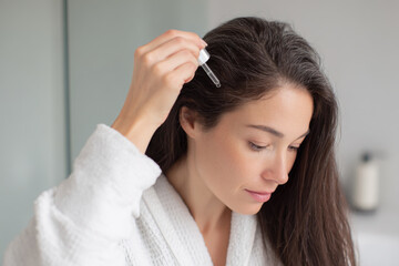 Woman applying hair serum to scalp for growth and beauty