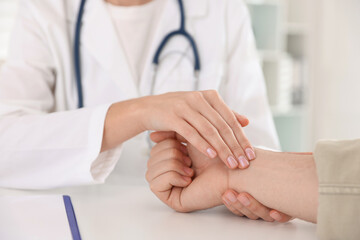 Doctor checking man's pulse with fingers at table in clinic, closeup