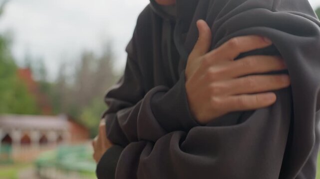 young man in hoodie clutching arm, outdoor park background, closeup hands pressing shoulder, chilly autumn light, introspective posture and vulnerability, casual streetwear, candid cinematic feel