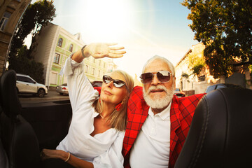 Stylish elderly couple enjoying ride in convertible car on sunny day, wide angle lens