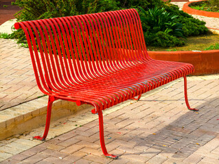 Worn red metal park bench with curved slats and peeling paint