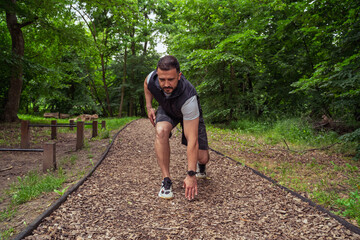 Man in standing start , on running path in the park or forest 