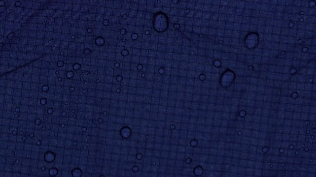 Water droplets on blue waterproof tent fabric texture during rain in landscape view