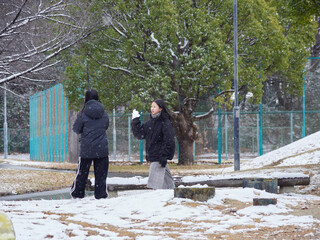 冬の朝の積雪の公園で楽しく雪合戦で遊んでいる子供姉妹の姿