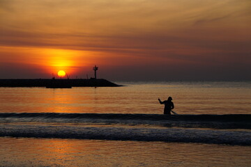 Fototapeta premium A fisherman nets fish at dawn. The sea is tinted golden by the sun rising over the horizon.The fisherman and the sea.