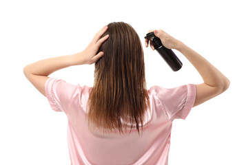 Young woman in pajamas applying hair spray on white background, back view