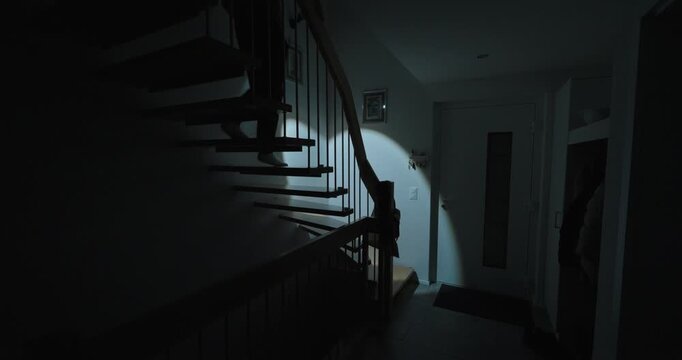 A person moves through a dark home staircase during a blackout, using a flashlight and candlelight for safe navigation.