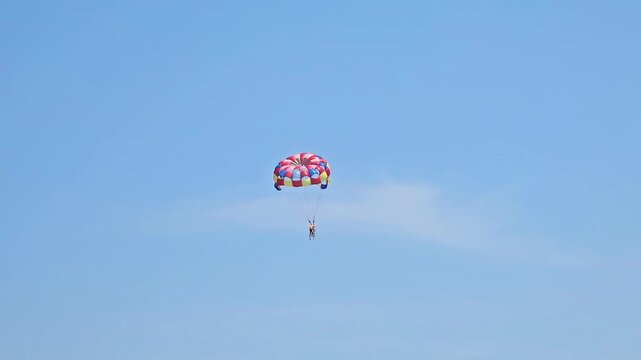 Person parasailing high in the clear blue sky, experiencing an exciting summer adventure, thrill, and freedom during watersport activity as part of fun beach vacation in Da Nang, Vietnam