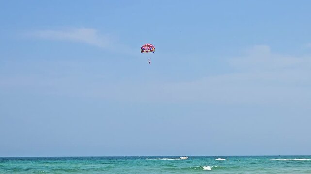 Person parasailing high in the clear blue sky, experiencing an exciting summer adventure, thrill, and freedom during watersport activity as part of fun beach vacation in Da Nang, Vietnam
