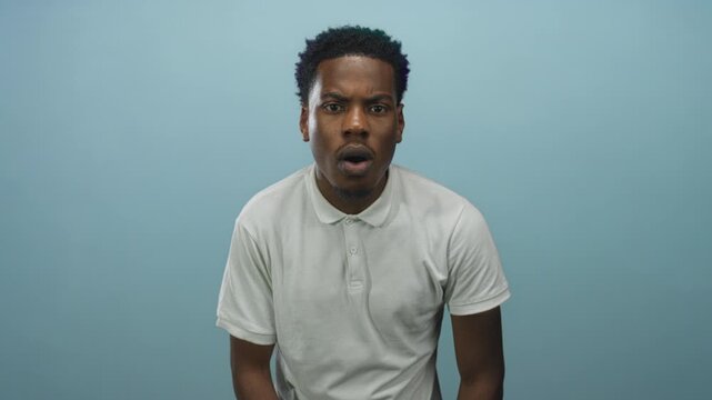 Young african american man with open mouth and raised eyebrows in studio wearing white polo shirt looking forward; surprise.