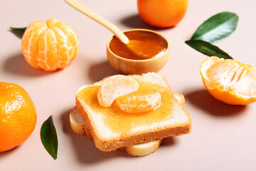 Bowl of tasty tangerine jam with toasts and leaves on beige background