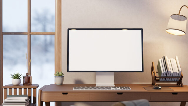 White screen computer with book rack and lamp on wooden table with snow falling outside glass window