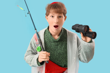 Funny young man with fishing rod and binoculars on blue background