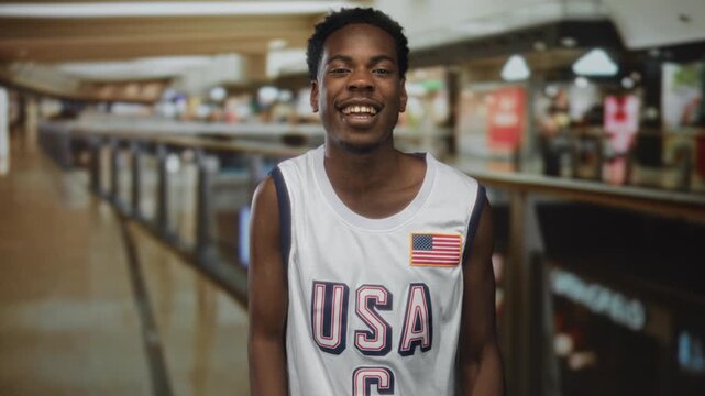 Man wearing white usa basketball jersey with american flag patch pumps fist with smiling face in building; excitement.
