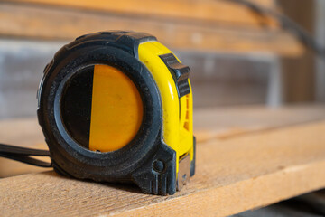 Black and yellow tape measure sitting on wooden board in a workshop setting