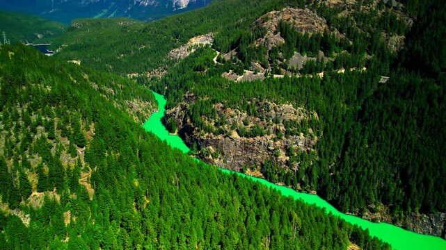 Aerial drone view of emerald green river flowing through forested canyon with winding mountain road near diablo lake in north cascades national park, washington