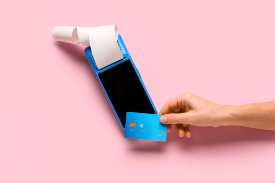 Female hand with credit card and payment terminal on pink background
