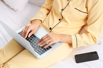 Young woman using laptop on bed in hotel room