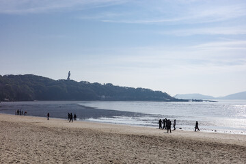 Tourists on the Beach with Distant Nanhai Guanyin Statue, Pilgrims, Coastal Scenery and Buddhist Landmark in One View. Mount Putuo, Zhoushan, Zhejiang, China