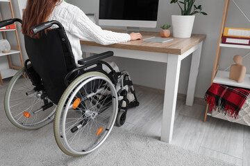 Fototapeta premium Woman in wheelchair working with computer at office, back view